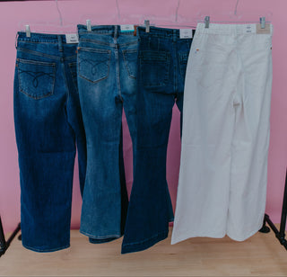 Four pairs of jeans, two blue and two white, hanging on a rack against a pink wall.